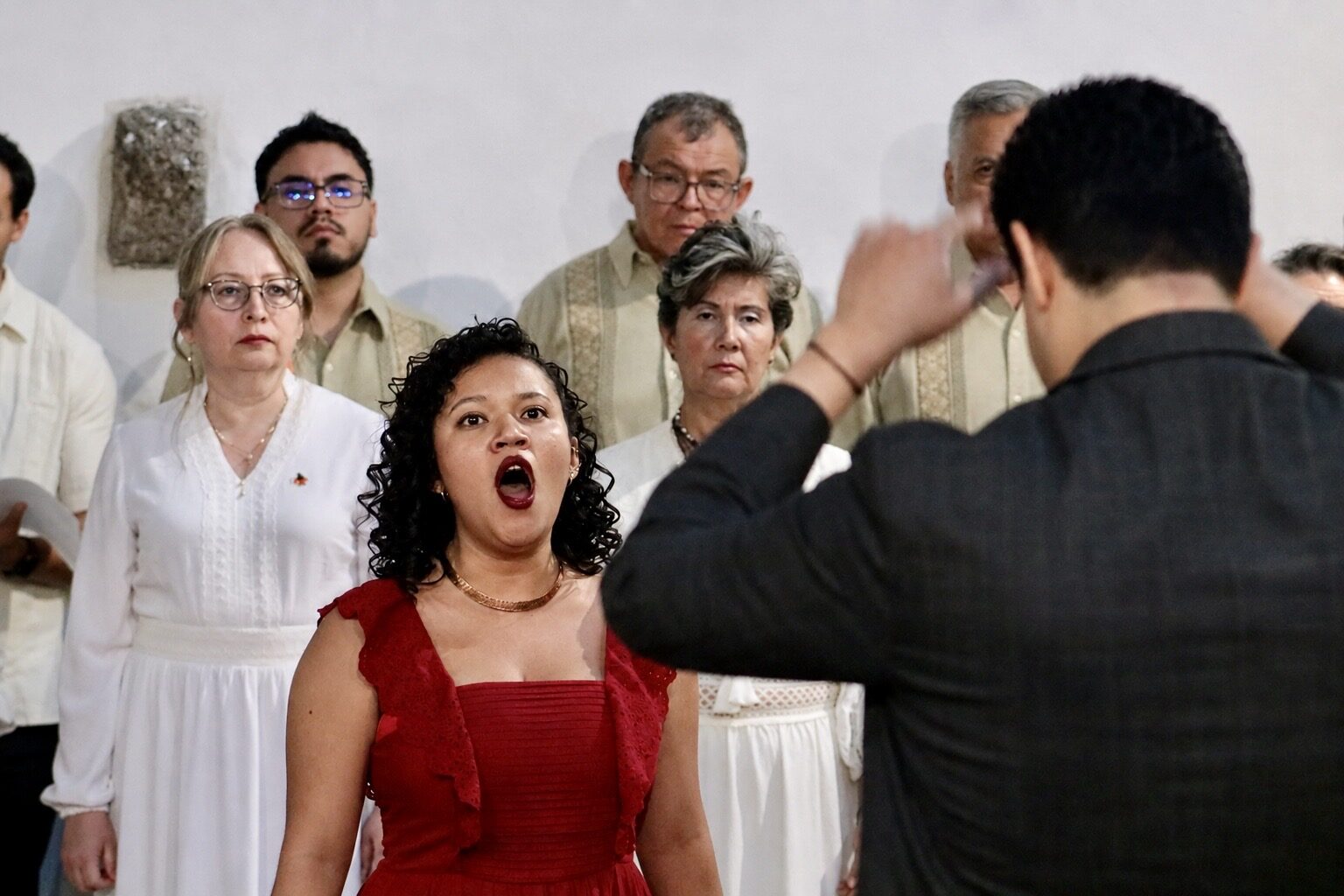 Natali Juárez en primerísimo plano cantando mientras Omar Nieto dirige